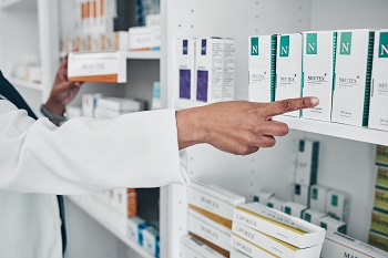 Pharmacy employee double checking the prescription to the drug on the shelf.