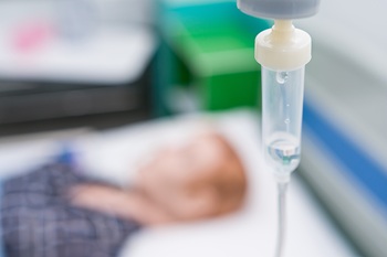 Closed-up of IV Solution with blurry sleeping patient in the hospital. Soft focus at infusion bottle.