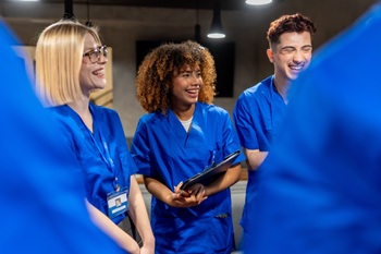 Diverse young medical students and healthcare trainees laughing together during a collaborative team discussion, showing camaraderie, support and joy in a clinical learning setting.
